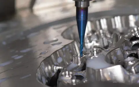 Fresa blu lavora un pezzo metallico, creando dettagli precisi. La cam meccanica è in azione, con liquido refrigerante che schizza.