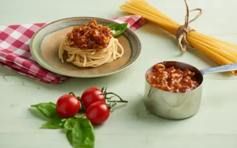 Pyszny sos do spaghetti z mięsem mielonym, podany na talerzu z makaronem, obok świeżych pomidorków i bazylii.
