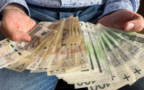 Ręce trzymające plik banknotów 100, 200 i 500 zł. Zastanawiasz się, do jakiej kwoty można zrobić przelew bez podatku?