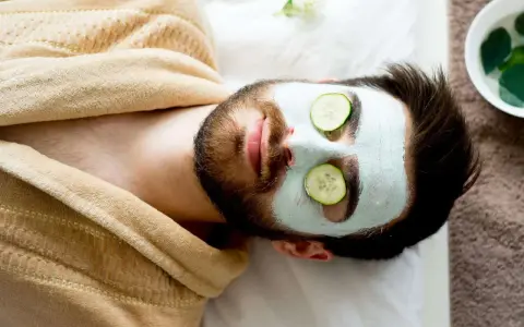 Man with a face mask and cucumber slices on eyes, relaxing. Wondering how long to keep face mask on for best results.