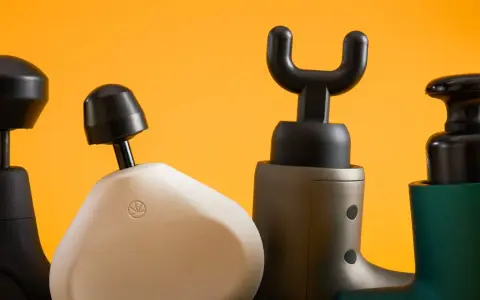 Four percussion massagers with different attachments are lined up against a bright orange background.