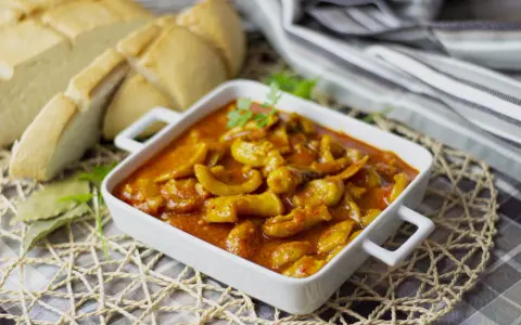 Delicioso plato de sepia en salsa, servido en cazuela blanca, acompañado de pan rústico y hojas de laurel.