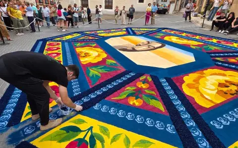 Un hombre finaliza una de las alfombras de serrín de Elche de la Sierra, con un retrato central y motivos florales y frutales.