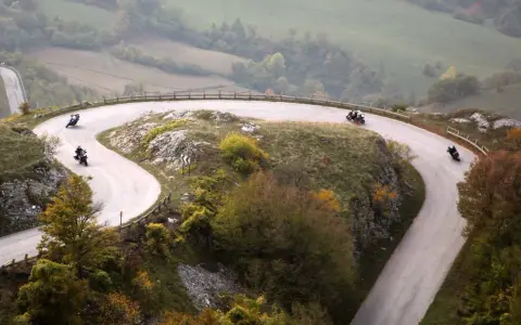 Motociclisti sfrecciano sulle curve delle Gole del Furlo, immersi in un paesaggio autunnale.