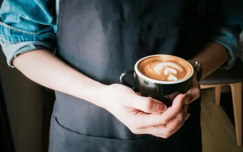 Barista hält eine Tasse mit Latte Art, die die perfekte Cortado Zubereitung zeigt.