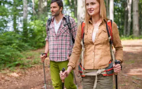 Ein Paar wandert achtsam durch einen Wald. Die Frau und der Mann nutzen Wanderstöcke, eine Anleitung für einen achtsamkeitsspaziergang.