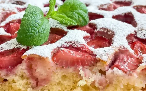 Szybkie ciasto z truskawkami, posypane cukrem pudrem i ozdobione listkiem mięty. Idealne na letnie popołudnie.
