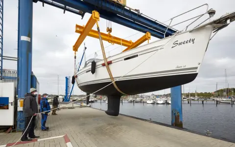 Segelboot "Sweety" wird für das unterwasserschiff reinigen aus dem Wasser gehoben. Männer sichern das Boot mit Seilen.