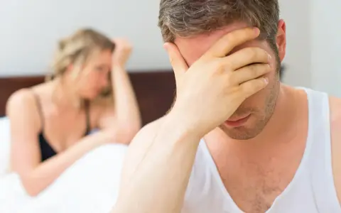 Mężczyzna w bieliźnie zakrywa twarz dłonią, kobieta w tle odwrócona.