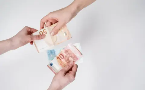 Dwie ręce przekazują sobie banknoty euro. To waluta Słowenii, używana do codziennych zakupów.
