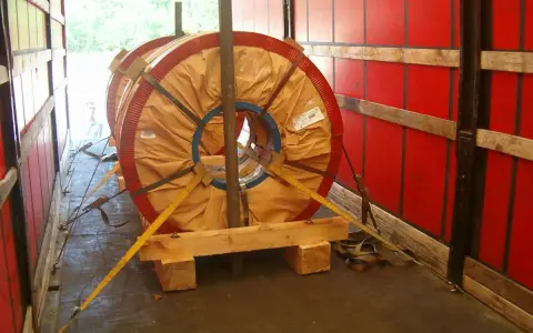 Dwa wielkie zwoje metalu zabezpieczone drewnianym mocowaniem blokowym i pasami transportowymi w naczepie.