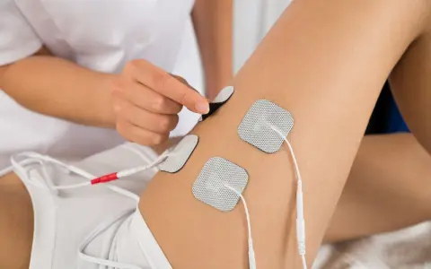 Terapeuta umieszcza elektrody na udzie pacjenta, przygotowując do zabiegu elektrostymulacji.