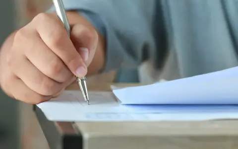 Dłoń trzymająca długopis, która wypełnia test. Czy przed jak również stawiamy przecinek, gdy piszemy.