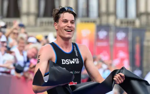 Lächelnder Athlet durchbricht die Ziellinie beim Triathlon Sprint, jubelnd mit schwarzem Band.