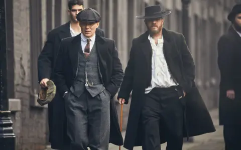 Tommy Shelby e altri uomini in abiti eleganti camminano per strada.
