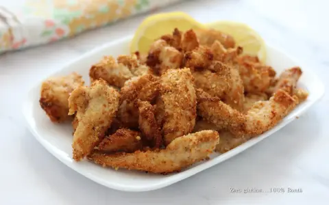 Straccetti di pollo in friggitrice ad aria, dorati e croccanti, serviti su un piatto bianco con spicchi di limone.