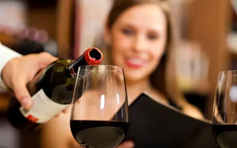 Kelner nalewa wino, a uśmiechnięta kobieta czeka na kieliszek. Wino zawiera siarczyny, które pomagają w jego konserwacji.