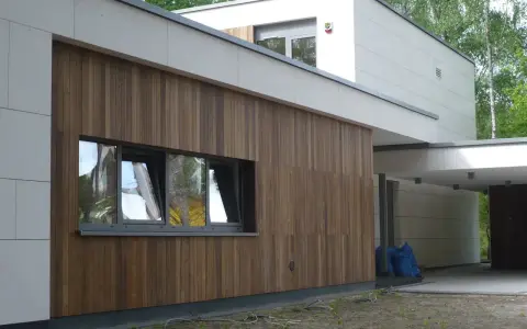 Nowoczesny dom z białymi panelami i elewacjami drewnianymi pionowymi. Okna odbijają drzewa.