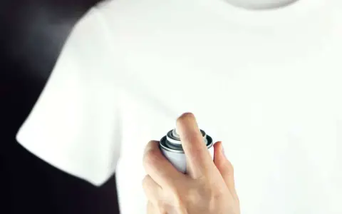 Hand sprüht mit einer Dose auf ein weißes T-Shirt, um statische Aufladung zu verhindern.