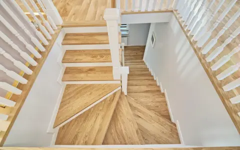 Eleganckie schody angielskie z drewna dębowego, z białymi balustradami, prowadzą w dół.