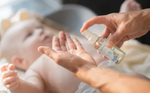 En hand sprutar olja i en annan hand, redo att smörja en bebis. Kanske för att lindra skorv bebis.