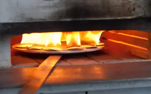 Des pièces de métal attendent d'être émaillées dans un four, sous des flammes vives. L'artisan émailleur surveille attentivement la cuisson.