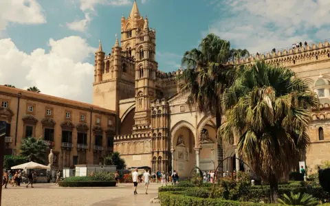 La Cattedrale di Palermo, un capolavoro di stili architettonici diversi, si erge maestosa sotto un cielo azzurro con palme rigogliose.