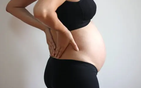 Gravid kvinna med handen på ryggen, upplever ont i ljumsken.