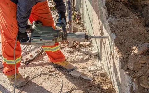 Trabajador con martillo neumático realiza demolición manual de muro de hormigón.