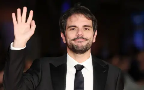 Valerio Vestoso saluta con la mano, sorridendo con un abito elegante.