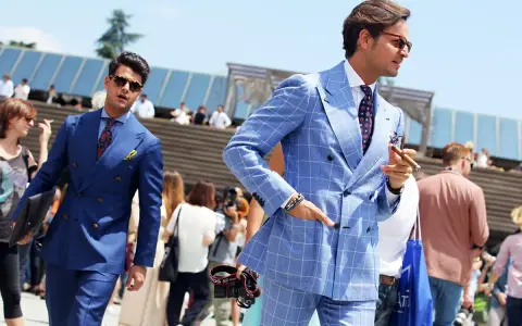 Dwóch eleganckich mężczyzn w garniturach prezentuje letnią modę męską. Jeden w niebieskim, drugi w błękitnym w kratę, obaj z pewnością siebie.
