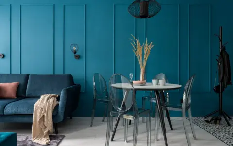 Soggiorno moderno con divano blu, tavolo rotondo con sedie trasparenti e pareti color ottanio.