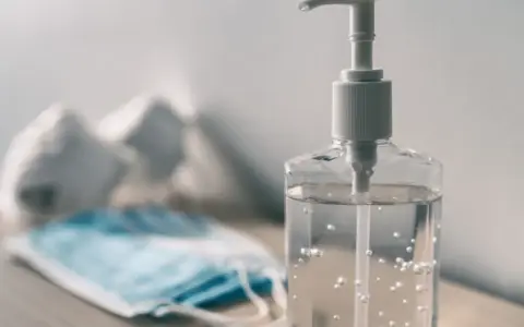 Butelka płynu do dezynfekcji i maseczka ochronna na stole.