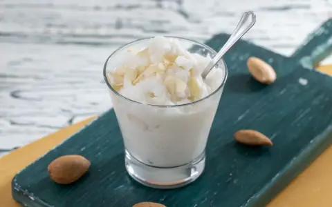 Rinfrescante granita alla mandorla, guarnita con lamelle di mandorle, servita in un bicchiere su un tagliere scuro.