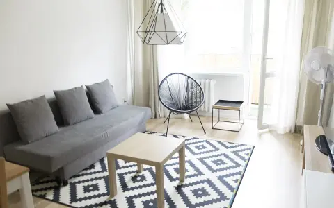 Nowoczesny salon z szarą kanapą i geometrycznym dywanem. Stylowa metamorfoza pokoju tanim kosztem.