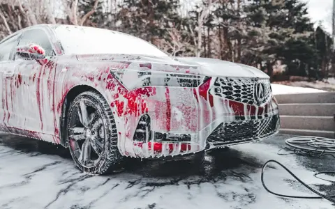 Czerwony samochód pokryty pianą, myty w zimnie. Czy można myc auto w mrozie? Tak, jeśli użyjesz odpowiednich środków.