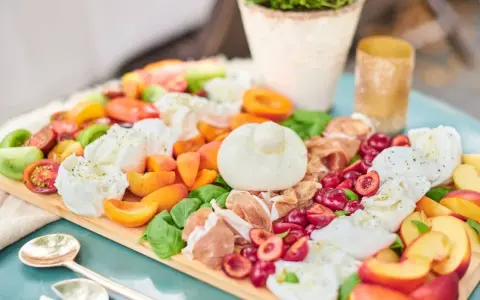 Eine üppige Antipasti Platte mit Burrata, Kirschen, Pfirsichen, Tomaten und Prosciutto.