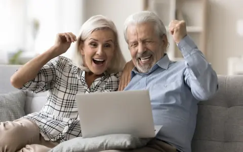 Szczęśliwi seniorzy sprawdzają na laptopie przeliczenie emerytury rocznik 1949 do 1953.