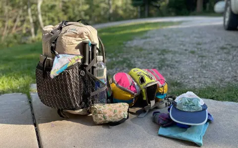 Backpack, water bottle, hiking poles, and colorful pouches are laid out, ready for a trip. This is how to pack light for an adventure.