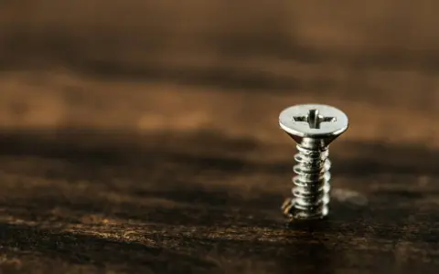 Un tornillo plateado sobre madera oscura. Para sacarlo, gira hacia la izquierda.