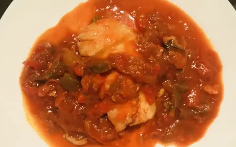 Un plato de urta a la roteña, con trozos de pescado blanco en una salsa roja de tomate y verduras.