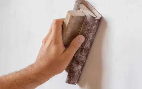 Mano lijando una pared con lija para pared y bloque de madera.