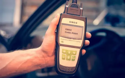 Hand holding an OBD2 scanner displaying code P0011, ready to diagnose car issues.