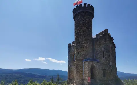 Kamienna wieża z polską flagą, część zamku księcia Henryka, góruje nad malowniczym krajobrazem gór i lasów.