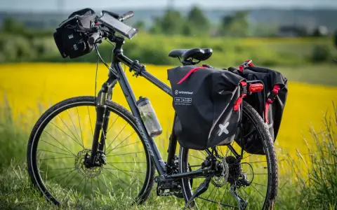 Gotowy na wyprawę rower z sakwami czeka na tle kwitnącego rzepaku.