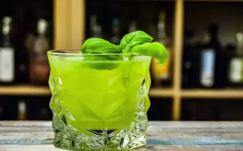 Orzeźwiający drink z likierem miętowym, ozdobiony listkami bazylii, w szklance o geometrycznym kształcie.
