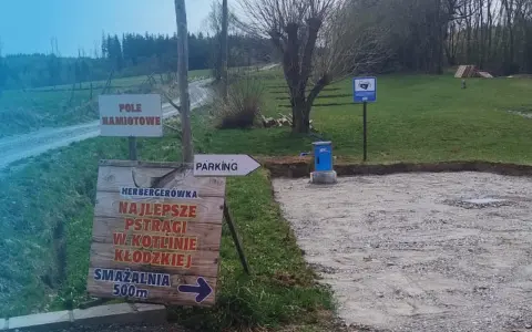 Miejsce na parking dla kamperów. Obok znak "Pole Namiotowe" i drogowskaz do smażalni pstrągów.
