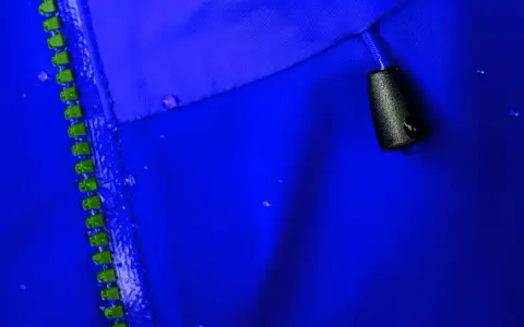 Nahaufnahme einer blauen Gore-Tex-Jacke mit Reißverschluss und Wassertropfen. So pflegt man Gore-Tex richtig beim Waschen.