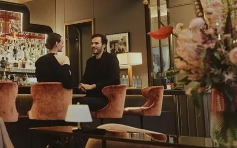 Para w eleganckim barze w Warszawie, uśmiechnięci, siedzą na aksamitnych stołkach. Idealna randka w stolicy.