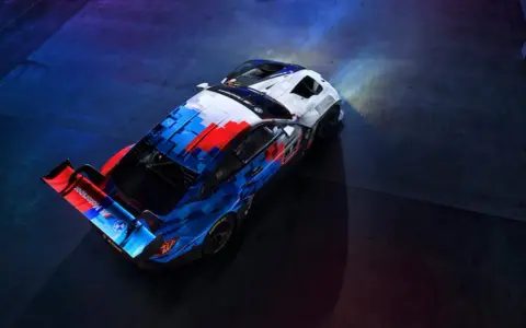 Der BMW M4 GT3 in dynamischer Motorsport-Lackierung steht bereit für die Rennstrecke, beleuchtet von Scheinwerfern.